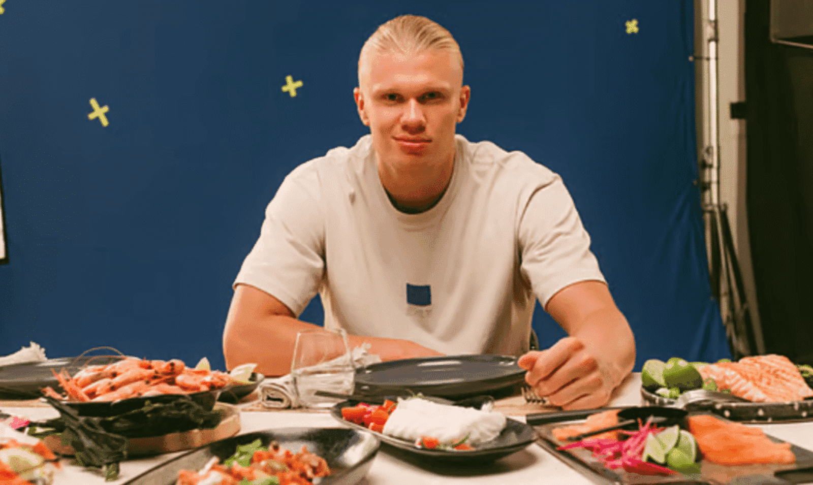 Erling Haaland sentado à mesa durante uma refeição com carnes, ovos, peixes, frutas e outros alimentos naturais que fazem parte de sua dieta.